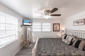 A bedroom with a bed, a ceiling fan, a television, and a window with blinds.