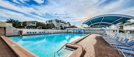 A swimming pool with a sunshade, lounge chairs, and a brick deck.