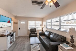 A living room with a couch, a chair, a coffee table, a TV, and a door with a beach-themed artwork.
