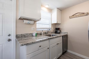 A kitchen with white cabinets, a granite countertop, a coffee maker, and a sign on the wall.