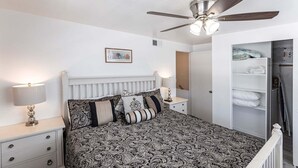 A bedroom with a bed, a ceiling fan, a nightstand, a lamp, a wardrobe, and a door leading to another room. - Aloha Kai Villa 50 - Premium Siesta Key Beach (Siesta Key)