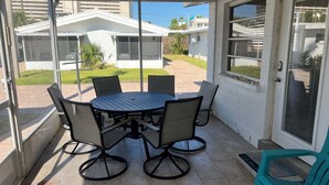 Een overdekt terras met een ronde tafel en stoelen, een deur met hor en een uitzicht op een woongebied.