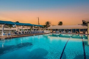 A swimming pool with lounge chairs and umbrellas, surrounded by buildings and palm trees.