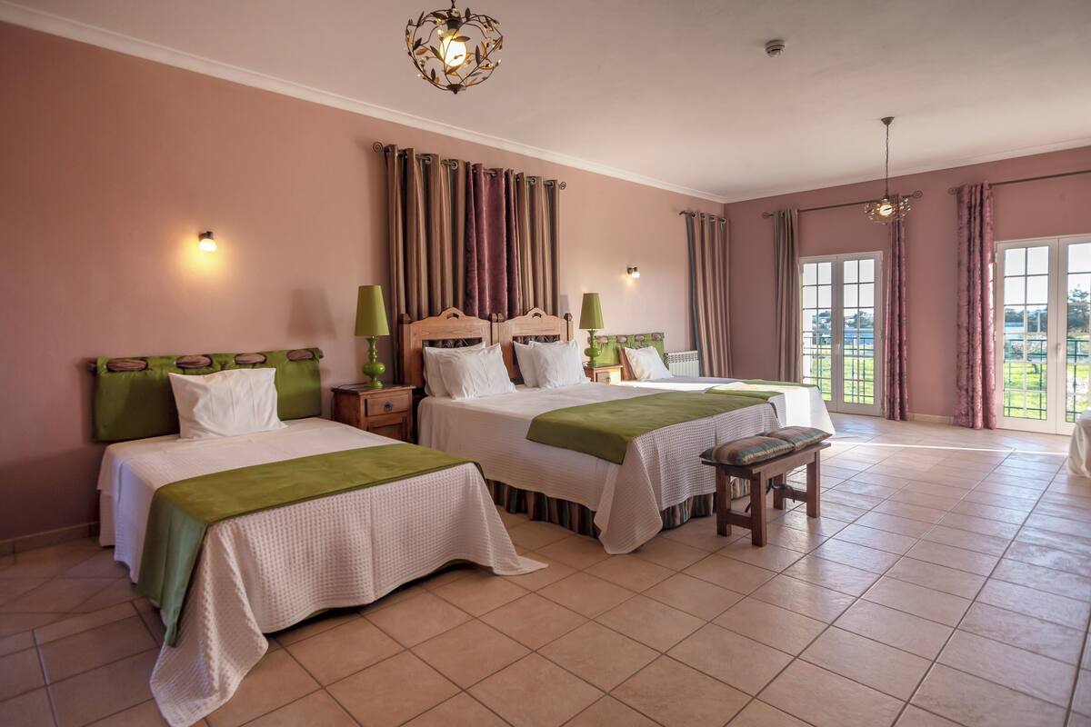 A hotel room with two beds, a bench, and a view of the outdoors.