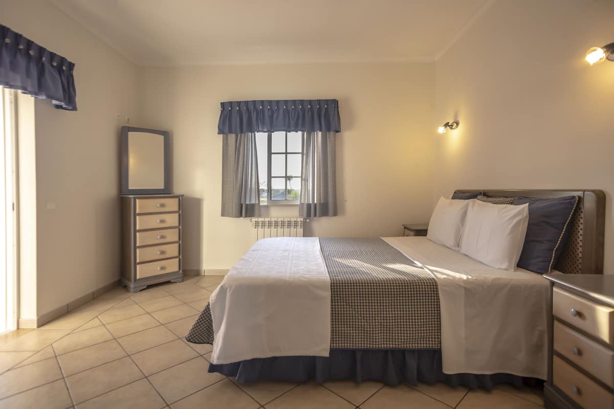 A bedroom with a bed, dresser, and a window with curtains.