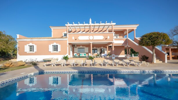 A large building with a swimming pool in front, featuring a covered patio area with lounge chairs and a staircase leading to the entrance. - Al Meida Guesthouse (Albufeira)