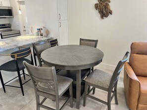 A modern dining area with a round table and four chairs, a kitchen with stainless steel appliances, and a decorative wall piece.