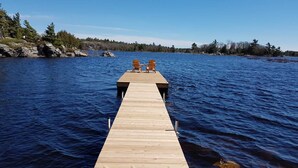 Un muelle de madera que se adentra en un lago, con dos sillas Adirondack al final.