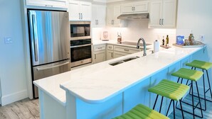 A modern kitchen with white cabinetry, stainless steel appliances, a large island with bar stools, and a built-in oven. - Unwind by the Beach in Orange Beach! 4 bed/3bath - Sleeps 8 - Oceanfront View (Orange Beach)
