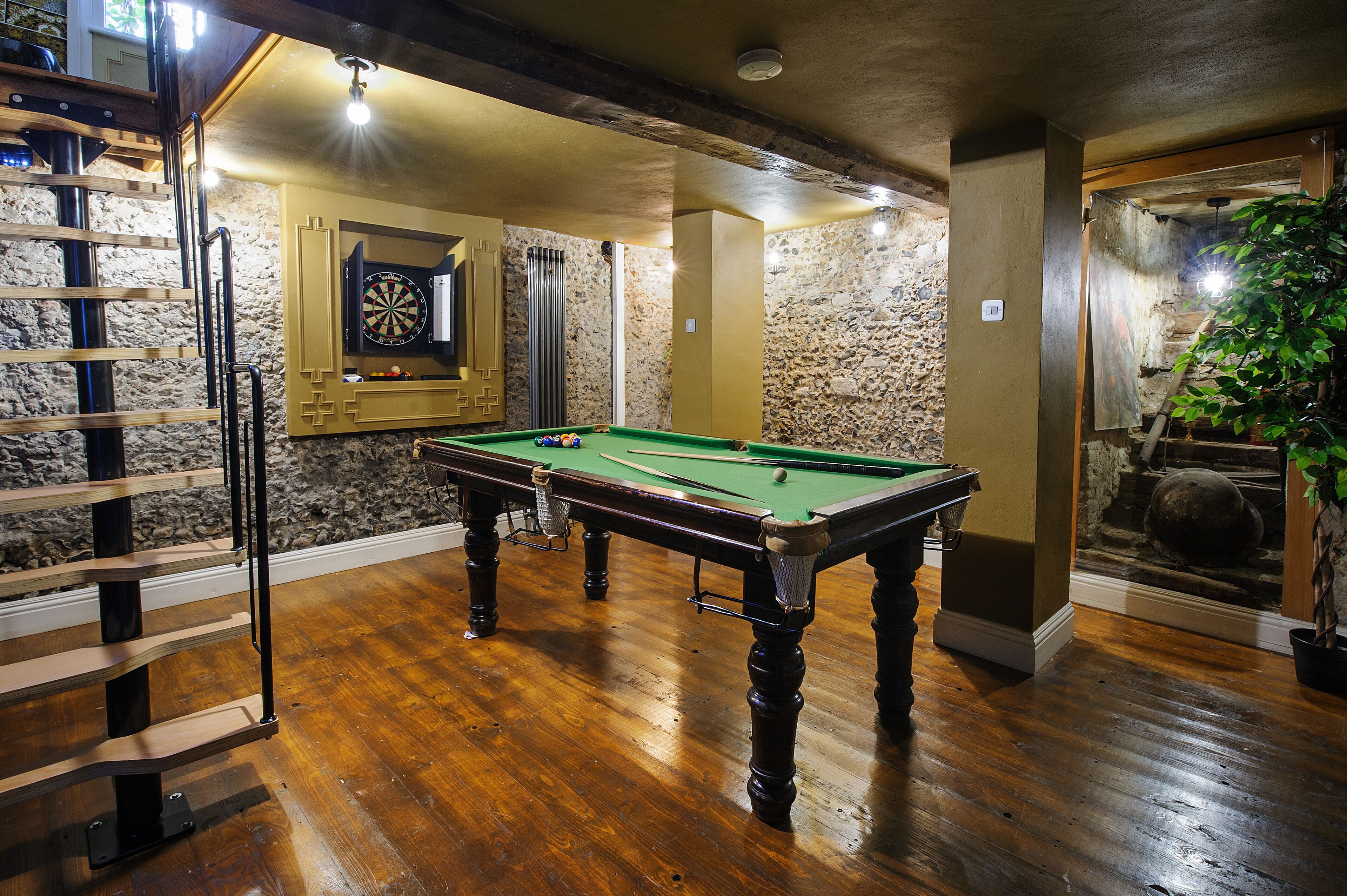 A billiards table in a room with stone walls, a wooden floor, and a dartboard on the wall.