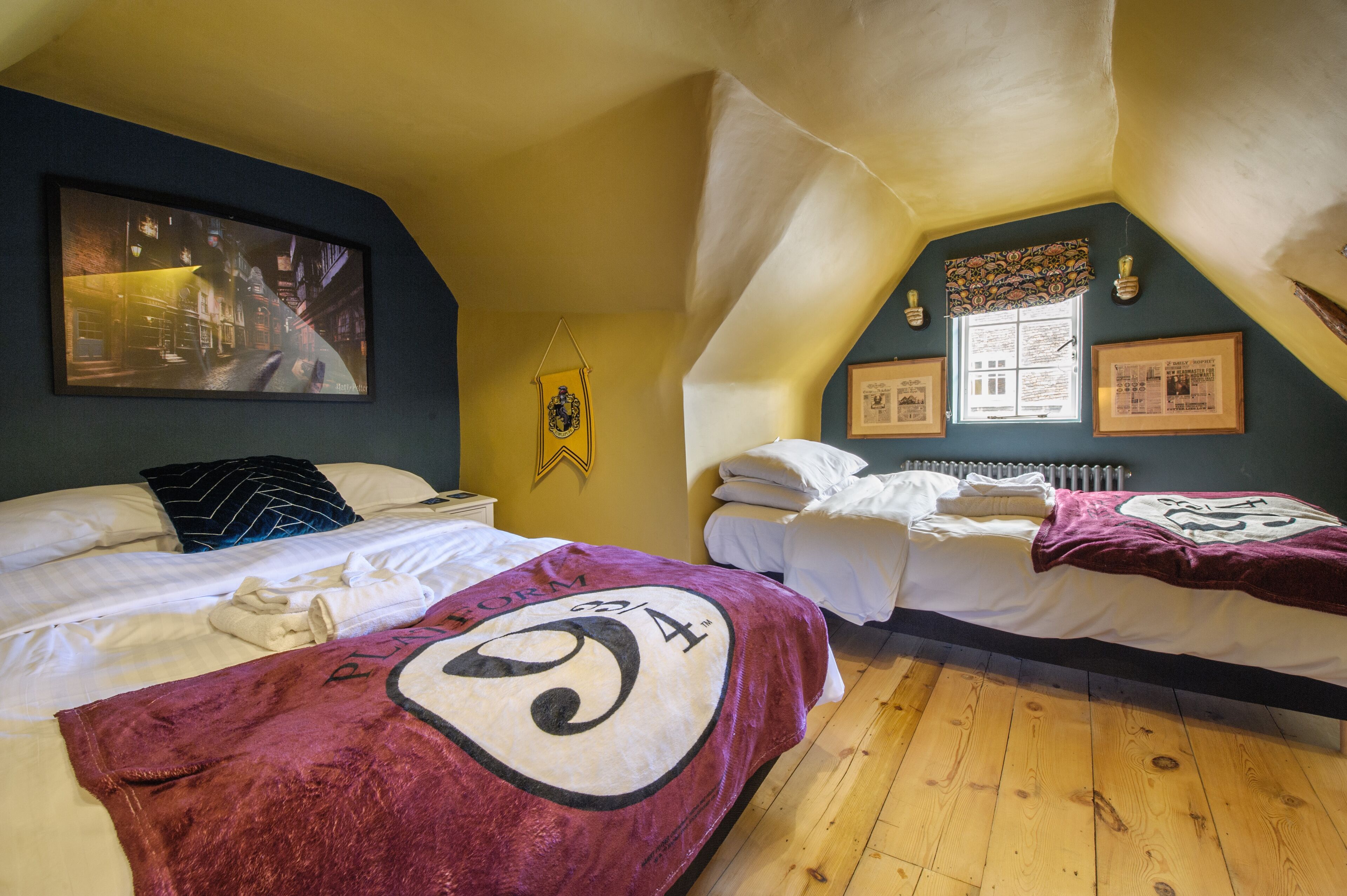 A room with two beds, a framed picture on the wall, and a window with a curtain.