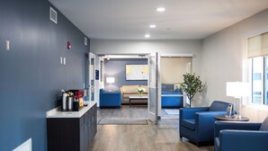 A modern hotel lobby with a blue wall, a reception desk, a sofa, a coffee table, and a plant. -  stayAPT Suites Columbus-Fort Benning (Columbus)