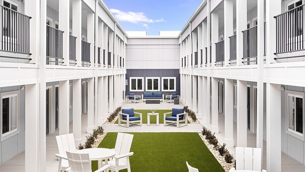 A modern courtyard with white furniture, a central seating area, and a small lawn. -  stayAPT Suites Columbus-Fort Benning (Columbus)