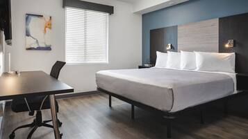 A modern hotel room with a large bed, a desk, and a window with blinds.