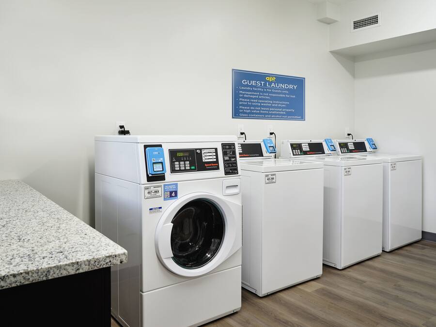 A laundry facility with four front-loading washing machines, a granite countertop, and a sign indicating it's for guests only.