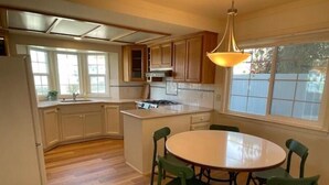 A kitchen with wooden cabinets, a round dining table with chairs, and a window providing natural light. - Fifth house from beach Avail June 14 - August18.  (Pismo Beach)