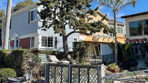 A residential area with a house featuring a large tree in front, a fenced yard, and a clear blue sky. - Fifth house from beach Avail June 14 - August18.  (Pismo Beach)