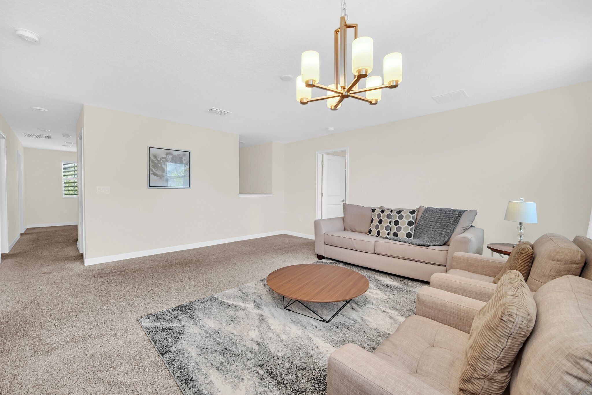Een ruime woonkamer met een beige bank, een ronde salontafel en een kroonluchter.