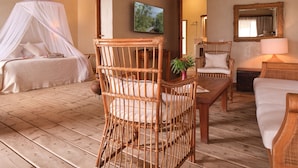 A room with a four-poster bed, a wicker chair, a sofa, and a wooden table.