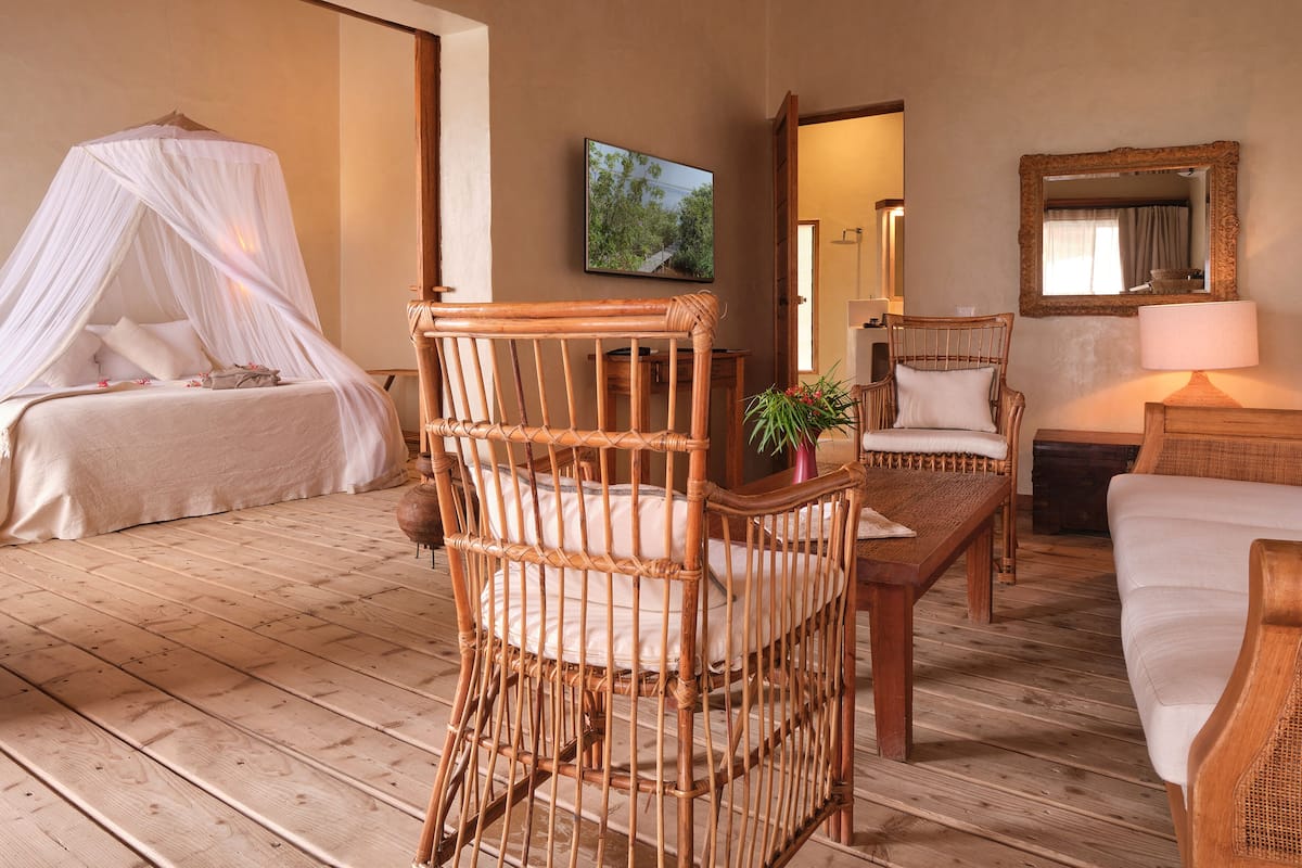 A room with a four-poster bed, a wicker chair, a sofa, and a wooden table.