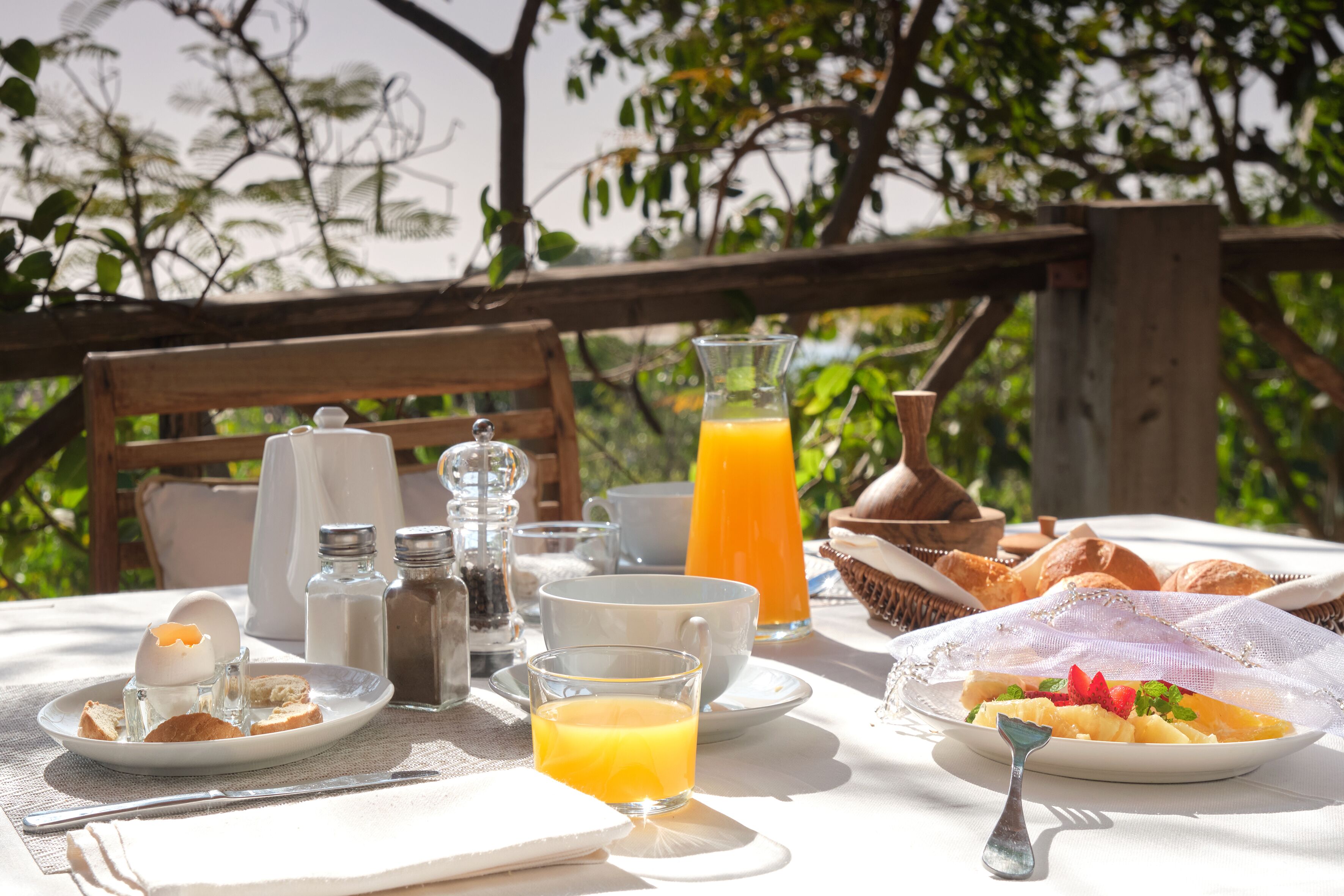 Una mesa de desayuno al aire libre con diversos alimentos, como tostadas, huevos y fruta, además de bebidas y salsas.