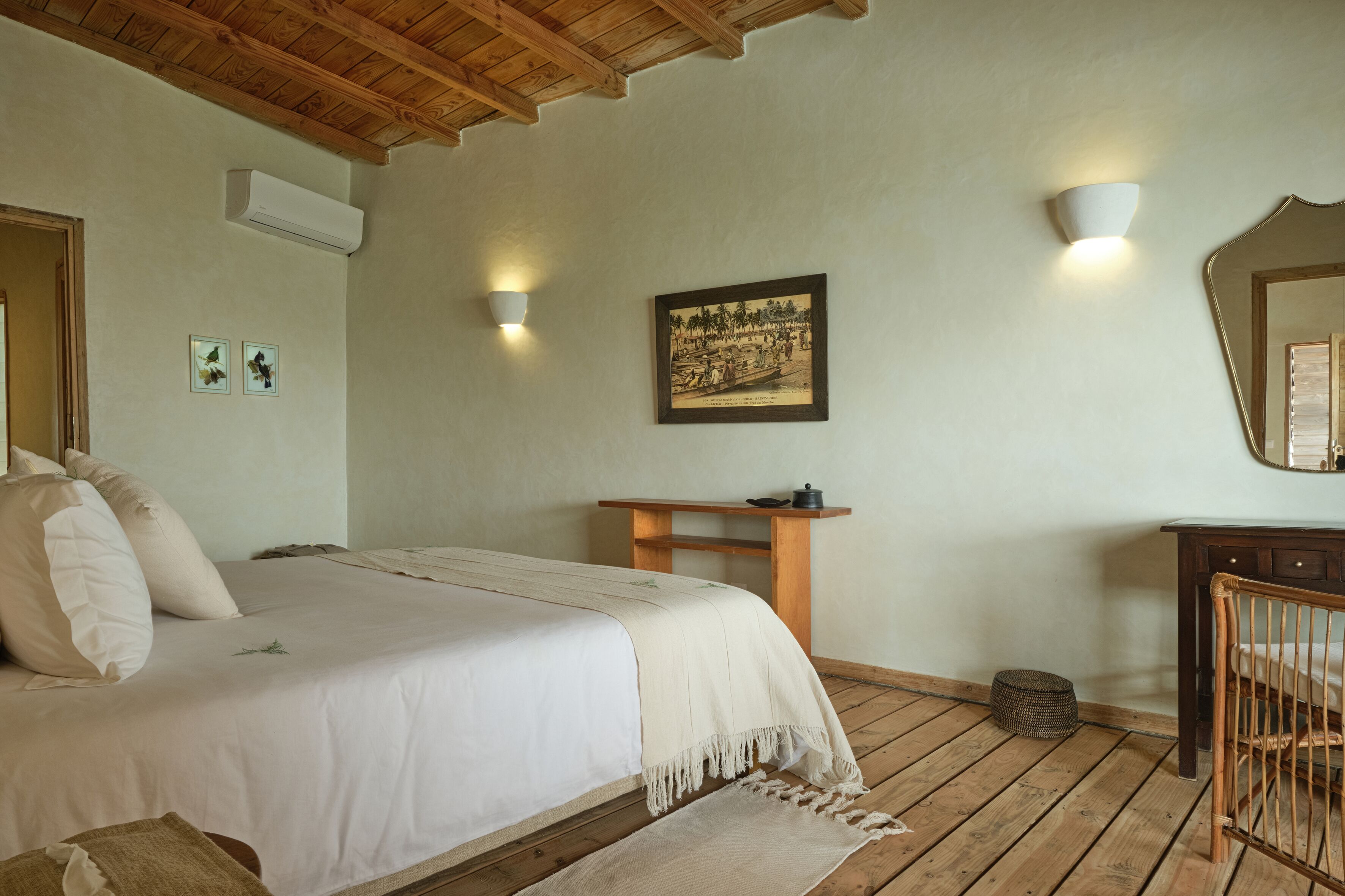 Een slaapkamer met een houten plafond, een bed met een witte dekbedovertrek, een nachtkastje met een lamp, een ingelijste foto aan de muur en een houten bureau met een stoel.