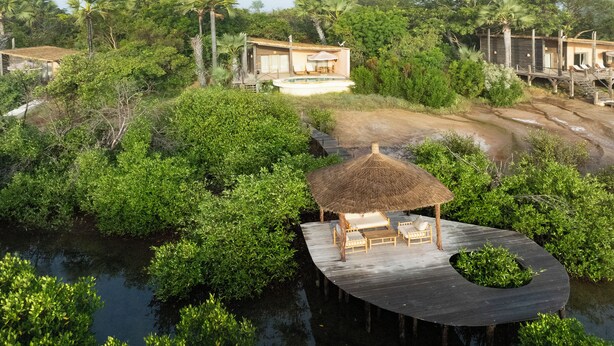 A secluded resort with a thatched-roof cabana on a wooden dock, surrounded by lush greenery and a calm water body.