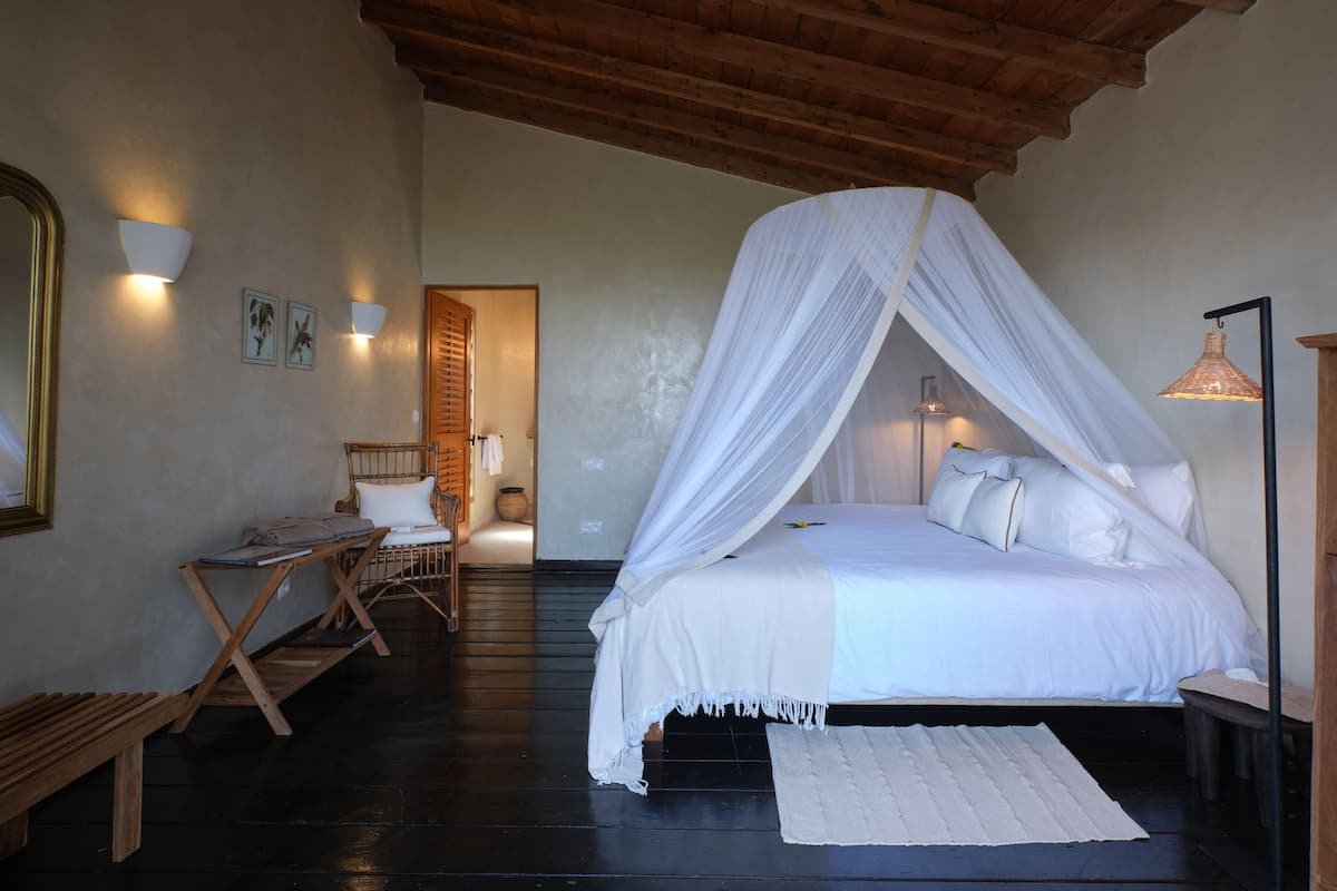 A bedroom with a canopy bed, wooden floor, and a bench.