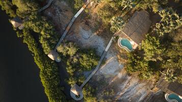 Eine Vogelperspektive zeigt ein Resort mit mehreren Schwimmbecken, einem Strandbereich und einer Holzbrücke, die verschiedene Bereiche miteinander verbindet.