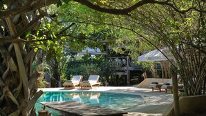 A pool area with lounge chairs, a wooden deck, and a covered seating area.