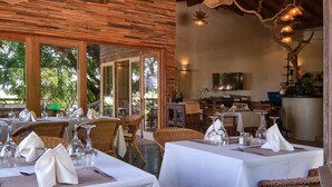 A restaurant with tables set for dining, wicker chairs, and a TV mounted on the wall.