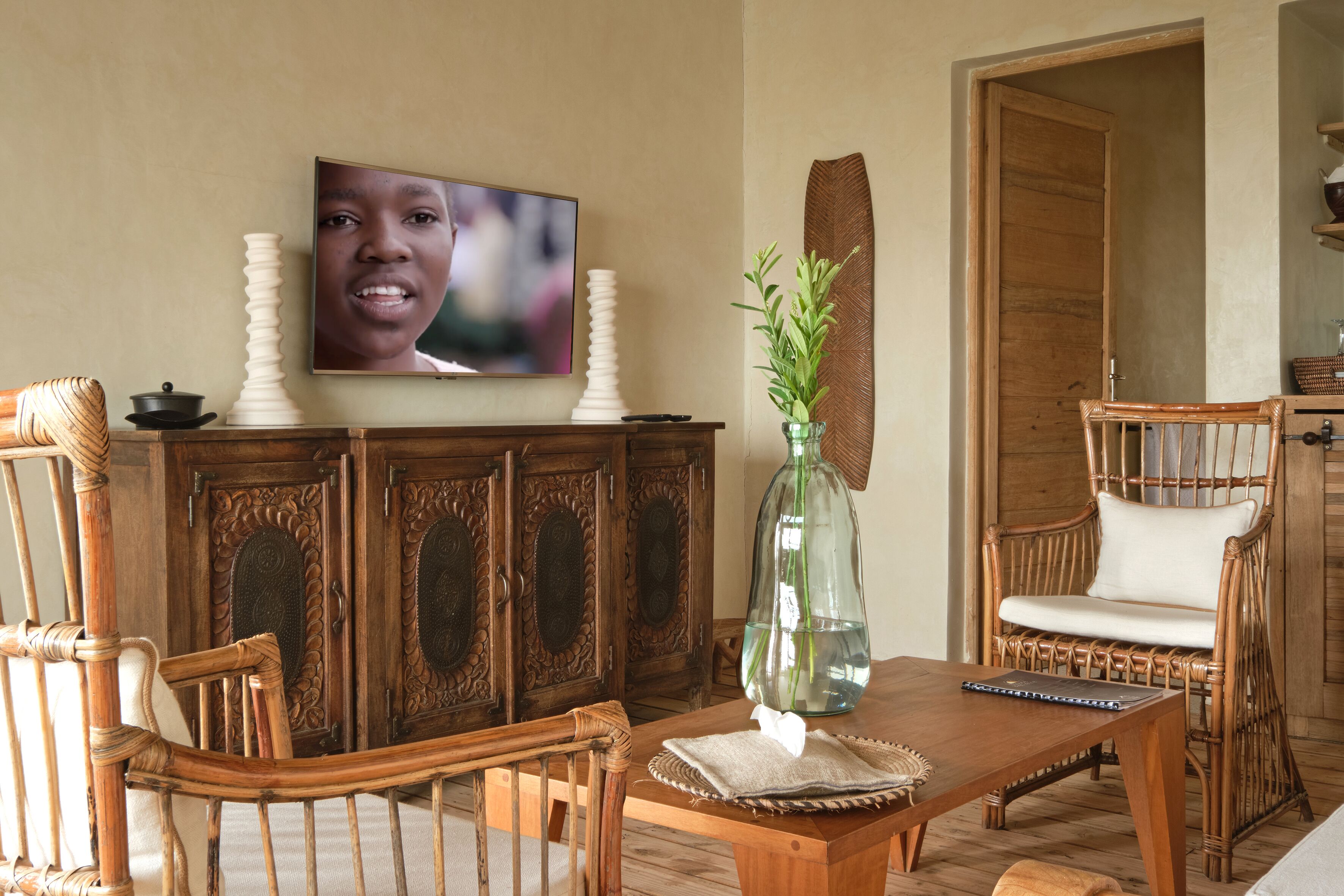 A wooden dining table with chairs, a television above it, and a decorative vase with plants.