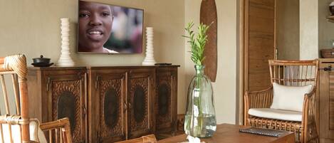 A wooden dining table with chairs, a television above it, and a decorative vase with plants.