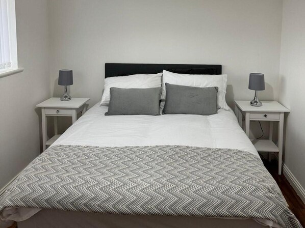 A neatly made bed with a patterned bedspread, two bedside tables with lamps, and a window with blinds.