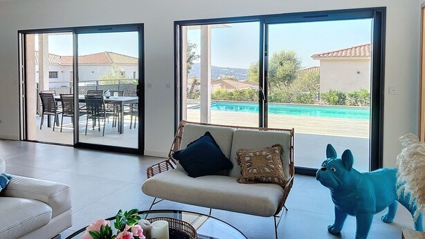 Ein geräumiges Wohnzimmer mit einer Couch, einem Couchtisch und einem großen Fenster mit Blick auf einen Swimmingpool und ein Gebäude.