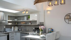 A modern kitchen with white cabinetry, a dining area with a table and chairs, and pendant lighting. - The Dairy, Newport - One Bedroom Cottage, Sleeps 2 (Newport)