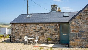 A stone building with a green door, a small patio with two white chairs and a table, and a view of the countryside. - The Dairy, Newport - One Bedroom Cottage, Sleeps 2 (Newport)