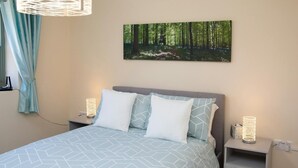 A bedroom with a bed, two bedside tables, a wall-mounted picture, and a hanging light fixture. - The Dairy, Newport - One Bedroom Cottage, Sleeps 2 (Newport)