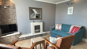 A living room with a stone fireplace, a flat-screen TV, a blue sofa, and a wooden coffee table. - Min y Graig, New Quay (New Quay)