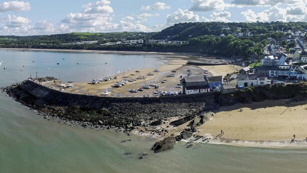 A coastal town with a sandy beach, a rocky breakwater, and boats docked near the shore. - Min y Graig, New Quay (New Quay)