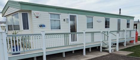 A mobile home with a fenced porch, windows, and a small sign.