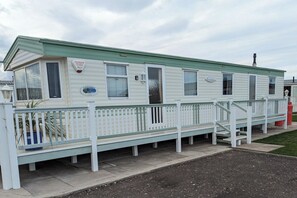 A mobile home with a fenced porch, windows, and a small sign. - Beach House Dog Friendly - Anderby Creek (Skegness)