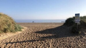 A beach with a sandy path leading to the sea, a signpost with information, and a few people in the distance. - Beach House Dog Friendly - Anderby Creek (Skegness)