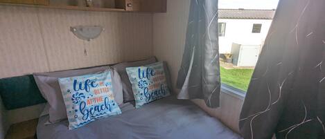 A bedroom with a bed, two pillows with text, a window with curtains, and a view of a house outside.