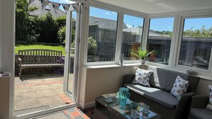 Une véranda avec une table en verre, un canapé en osier et une vue sur un jardin.