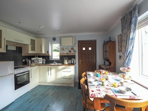 A kitchen with a dining table, wooden chairs, and a window with curtains.