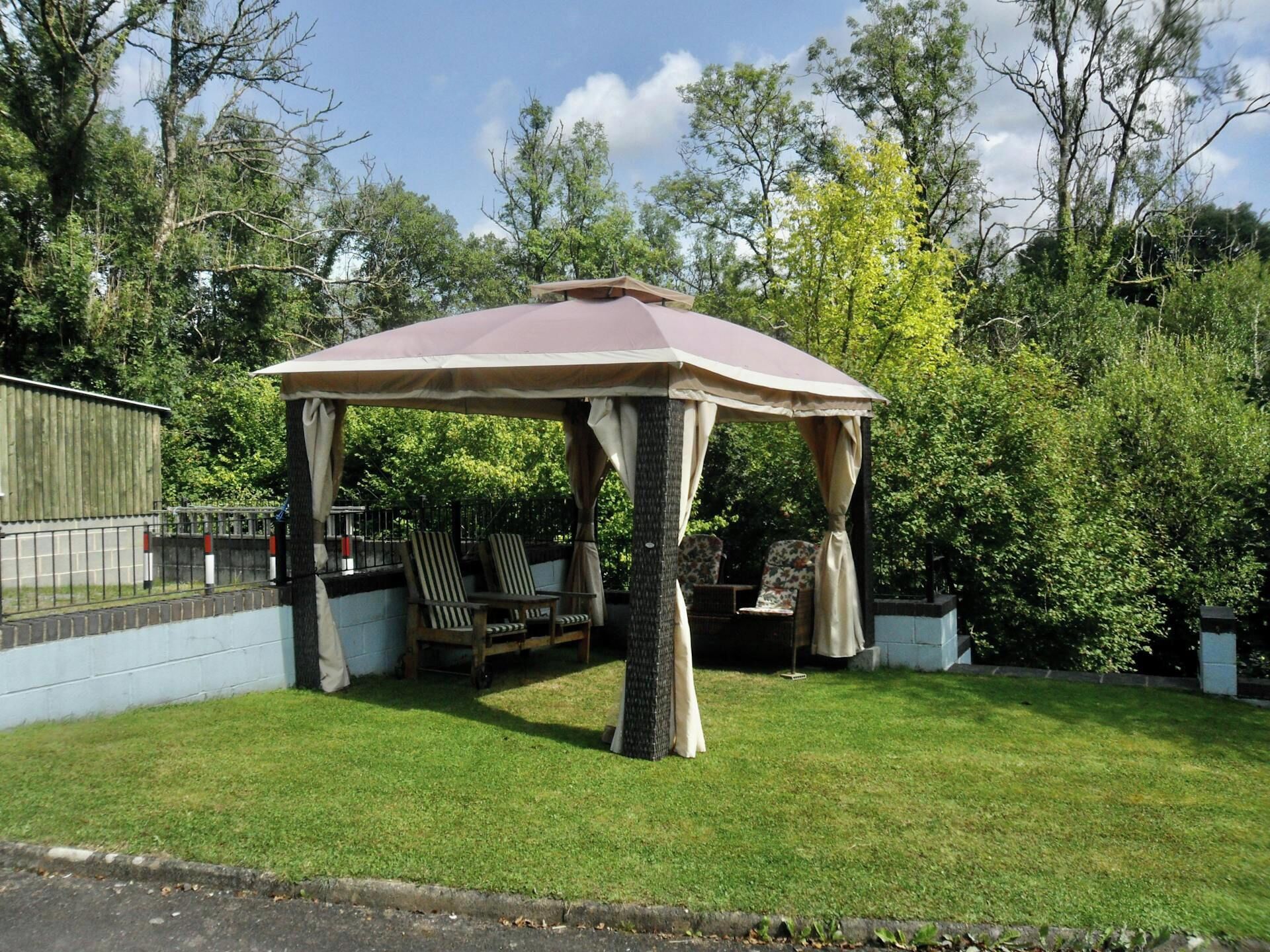 A gazebo with a roof, surrounded by grass and trees.