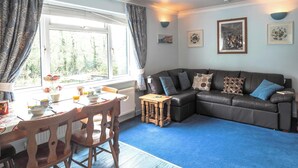 A living room with a sofa, a dining table with chairs, a radiator, and a window with curtains. - The Annexe, Llandysul (Penrhiw-llan)
