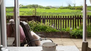 Un patio con una mesa, sillas y vistas a un campo verde con ovejas.
