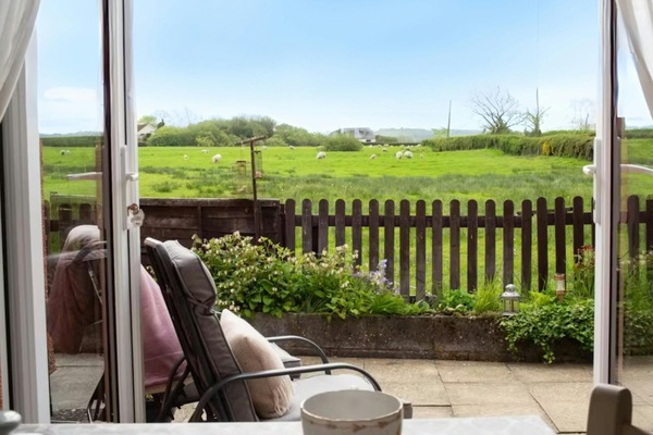 Patio doors leading to outside area with outdoor seating and view of fields with sheep